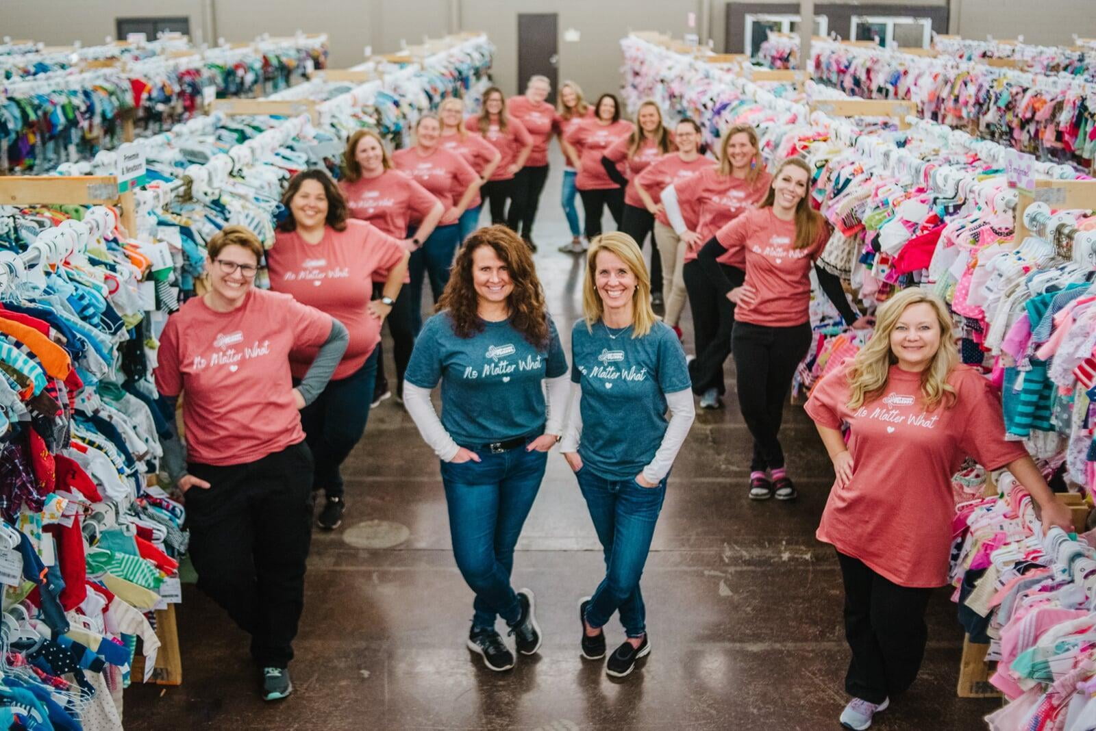 A mom and her three kids stand in front of a rack of girls clothes at their local BF sale.